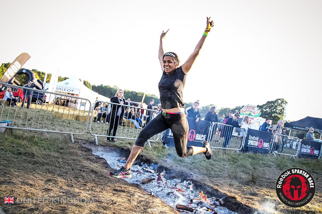 indian woman covered in mud jumping across a fire