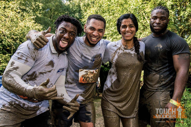 group of three black men and one indian woman covered in mud