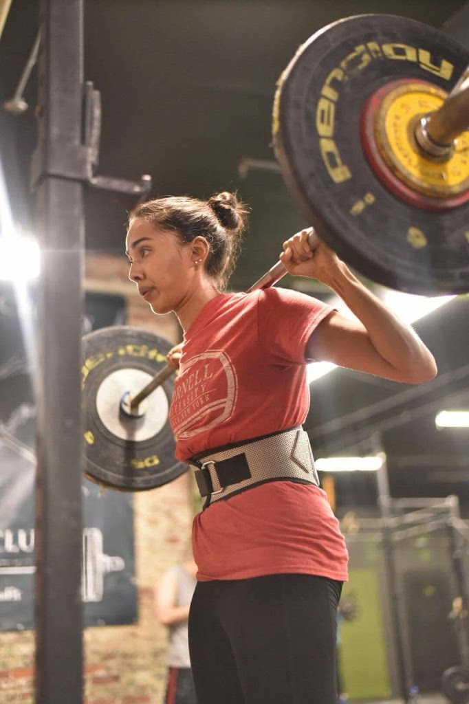 indian woman wearing a weightlifting belt, holding heavy barbell for a squat